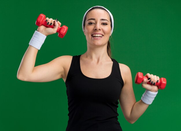 Jovem alegre e bonita e esportiva usando bandana e pulseiras segurando halteres