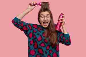 Foto grátis jovem alegre e emotiva penteia franja, usa laca para fazer um lindo penteado, surpreendida ao receber convite na festa, prepara