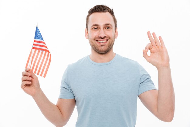 jovem alegre em camiseta casual, segurando a pequena bandeira americana e gesticulando sinal OK