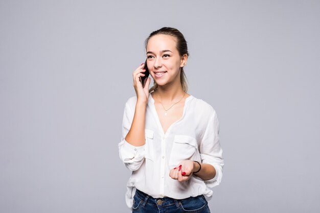 Jovem alegre falando no celular, isolada em uma parede cinza