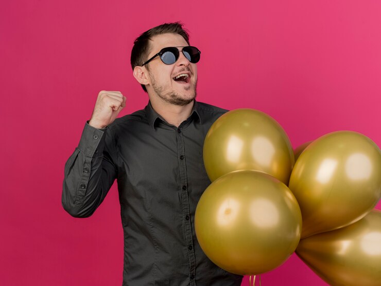 Foto grátis jovem alegre festeiro de óculos segurando balões mostrando gesto de sim isolado em rosa