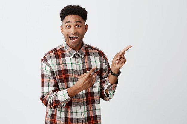 Jovem alegre linda cara de pele escura com cabelo encaracolado escuro bonito no casual penteado xadrez sorrindo, olhando de lado com expressão feliz e animada. Copie o espaço
