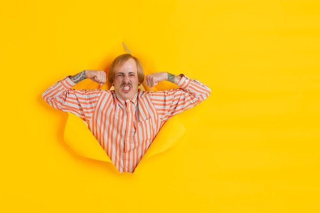 Jovem alegre posa emocionalmente e expressivamente na parede do buraco do papel amarelo rasgado