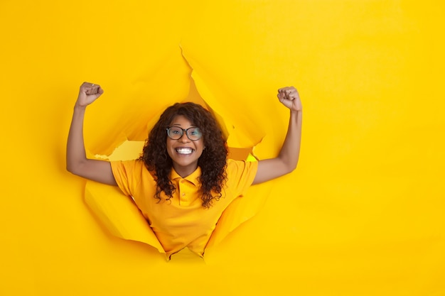 Jovem alegre posa no fundo do buraco de papel amarelo rasgado, emocional e expressivo