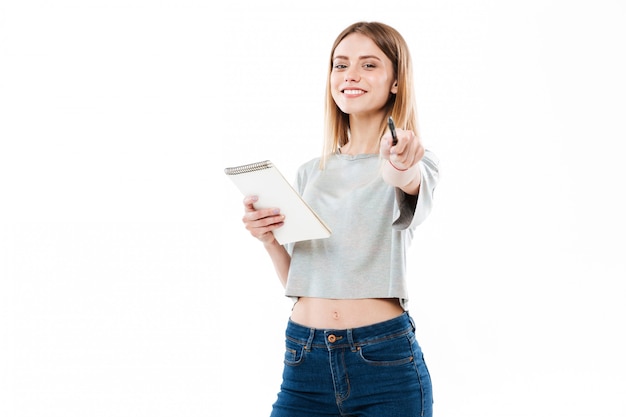 Foto grátis jovem alegre segurando o bloco de notas e apontando a caneta na frente