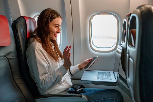 Jovem alegre usando laptop e celular no avião