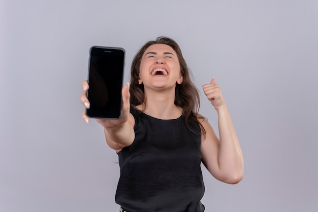 Foto grátis jovem alegre vestindo camiseta preta segurando o telefone para frente na parede branca