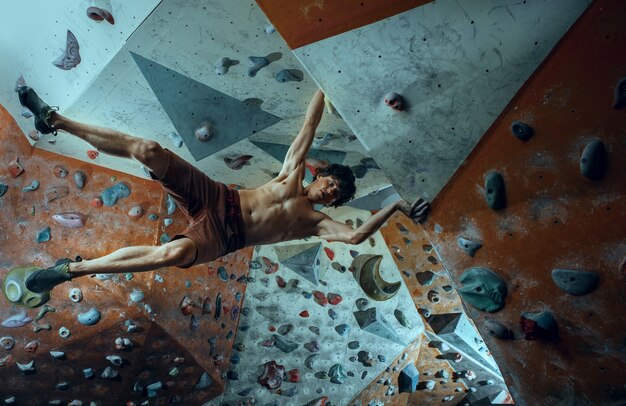 Jovem alpinista grátis escalando pedra artificial dentro de casa