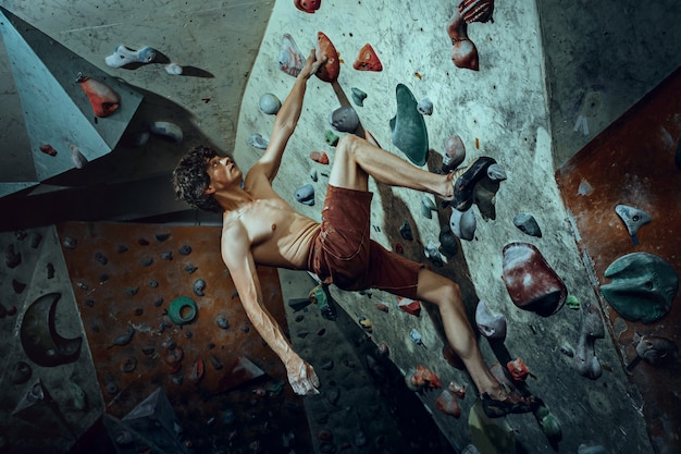 Foto grátis jovem alpinista grátis escalando pedra artificial dentro de casa