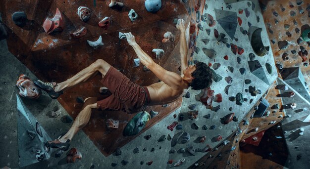 Jovem alpinista grátis escalando pedra artificial dentro de casa