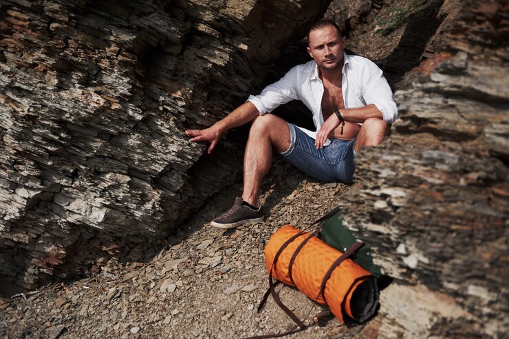 Foto grátis jovem alpinista masculina com mochila relaxante em um maciço rochoso durante o pôr do sol calmo de verão. conceito de férias viagem aventura estilo de vida