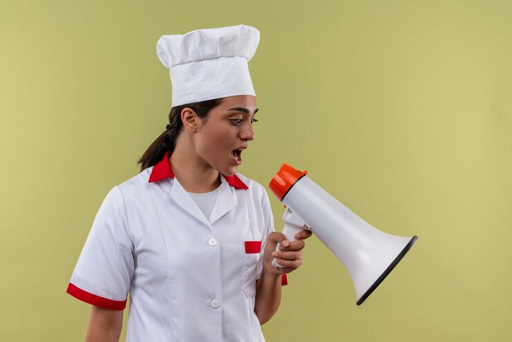 Foto grátis jovem ansiosa cozinheira caucasiana com uniforme de chef grita pelo alto-falante, isolada em um fundo verde com espaço de cópia