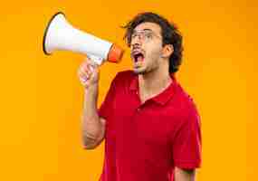 Foto grátis jovem ansioso de camisa vermelha com óculos ópticos gritando pelo alto-falante isolado na parede laranja