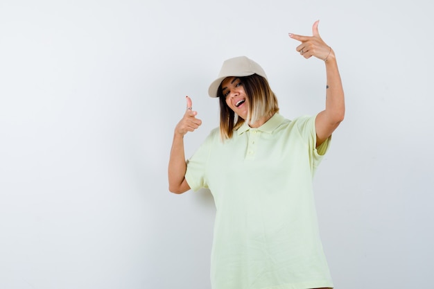 Jovem apontando de lado em t-shirt, boné e parecendo feliz. vista frontal.