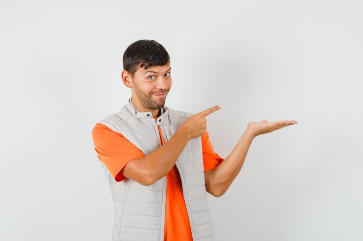 Foto grátis jovem apontando de lado, fingindo segurar algo do outro lado na camiseta, jaqueta e parecendo alegre.