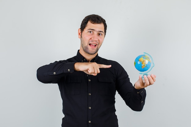 Jovem apontando o dedo para o globo em uma camisa preta e parecendo alegre