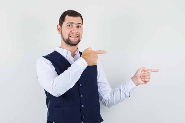 Jovem apontando os dedos para o lado em uma camisa, colete e olhando positivamente