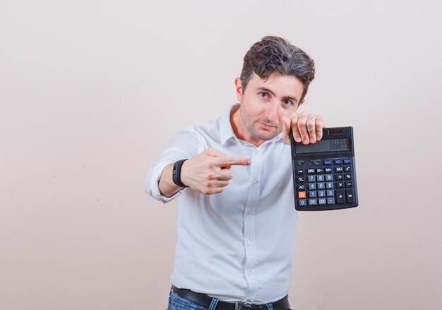 Jovem apontando para a calculadora de camisa branca, jeans e parecendo confiante