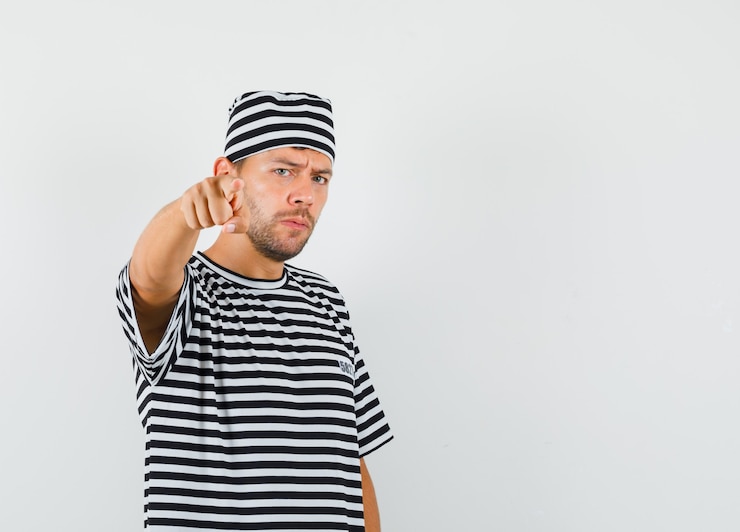 Foto grátis jovem apontando para a câmera com um chapéu de camiseta listrada e olhando sério