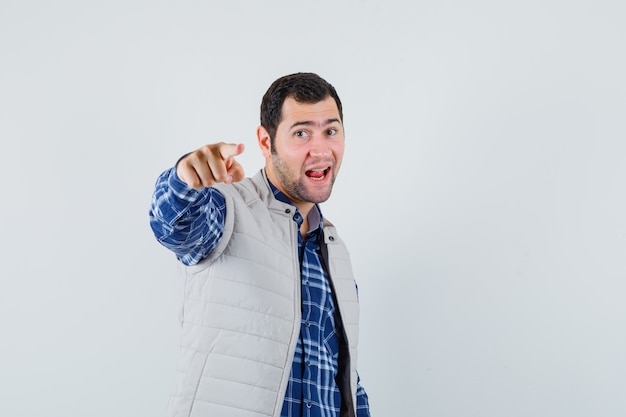 Jovem apontando para a câmera com uma camisa, uma jaqueta sem mangas e parecendo focado