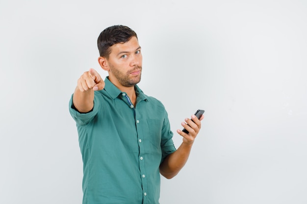 Jovem apontando para a câmera enquanto segura o smartphone na camisa