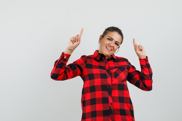 Foto grátis jovem apontando para cima com uma camisa xadrez e parecendo alegre