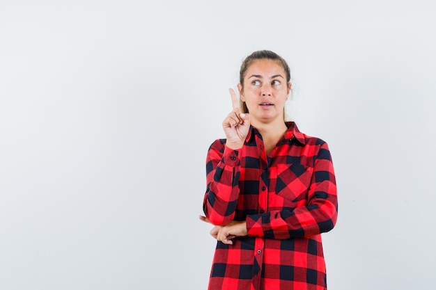 Foto grátis jovem apontando para cima com uma camisa xadrez e parecendo pensativa