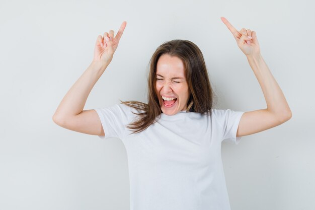 Jovem apontando para cima enquanto grita com uma camiseta branca e parece feliz