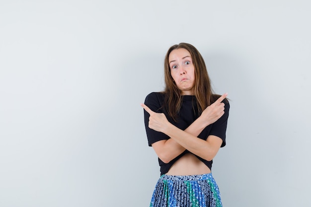 Foto grátis jovem apontando para longe com blusa, saia e parecendo confusa