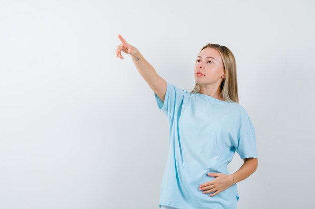 Jovem apontando para longe com uma camiseta e parecendo confiante isolada