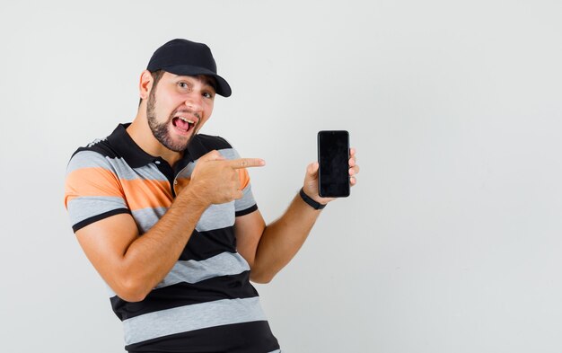 Jovem apontando para o celular de camiseta, boné e parecendo otimista