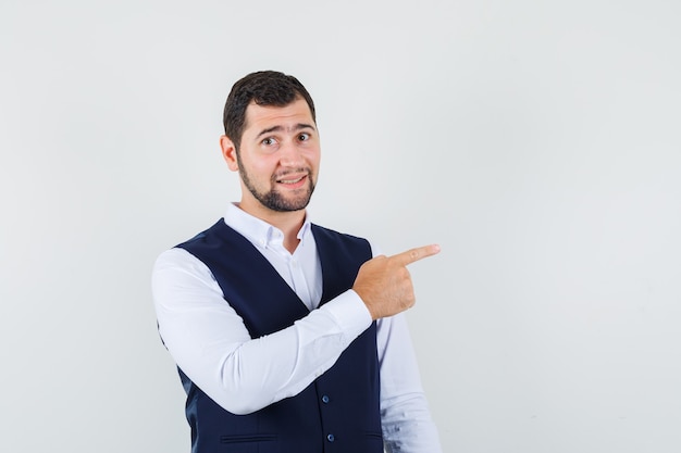 Jovem apontando para o lado com camisa, colete e parecendo preocupado