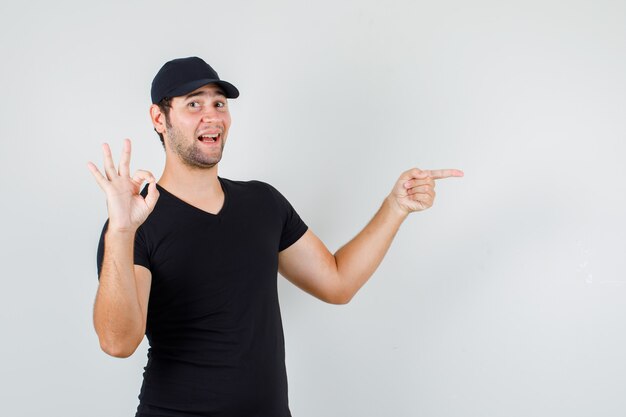 Jovem apontando para o lado com sinal de ok com camiseta preta