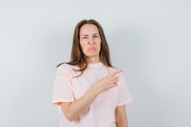 Jovem apontando para o lado com uma camiseta rosa e parecendo enojada