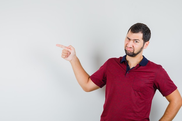 Jovem apontando para o lado em uma camiseta vermelha e olhando descontente, vista frontal.