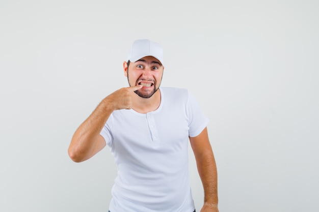 Jovem apontando para os dentes em uma camiseta e olhando com foco, vista frontal.