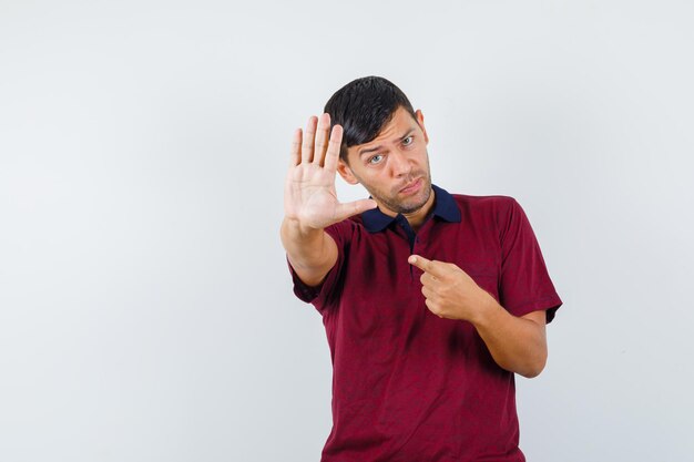 Jovem apontando para seu gesto de parada em t-shirt e olhando sério. vista frontal.