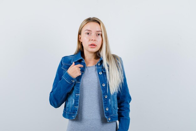 Jovem apontando para si mesma em camiseta, jaqueta jeans, saia e parecendo confiante