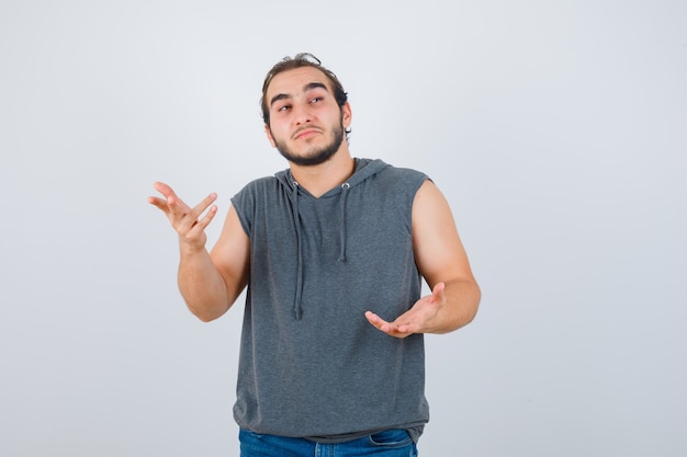 Foto grátis jovem apto masculino com capuz sem mangas, esticando a mão de maneira questionadora e parecendo pensativo, vista frontal