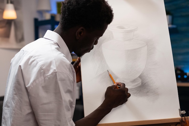 Jovem artista desenhando vaso fazendo sombras usando lápis gráfico profissional trabalhando em ilustração criativa para aula de arte. estudante de homem concentrado pintando em tela esboçando desenhar