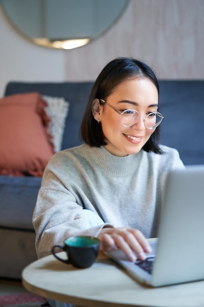 Foto grátis jovem asiática freelancer profissional sentada na sala de estar e trabalhando com computador estudando um