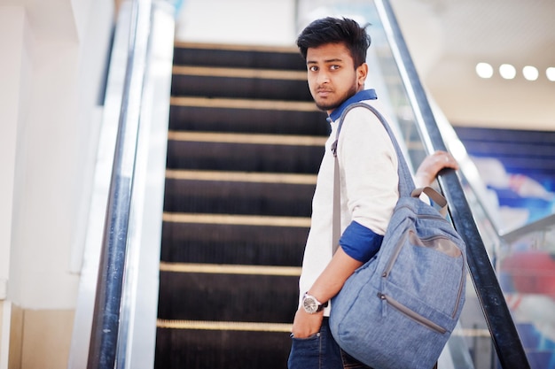 Jovem asiático com mochila se move na escada rolante no shopping