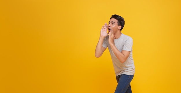 Jovem asiático gritando boca aberta levantando as mãos gritando anúncio para o espaço vazio de lado