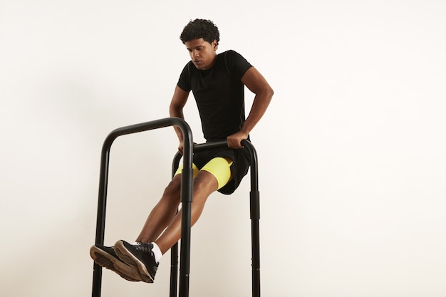 Jovem atleta afro-americana focada em roupas esportivas pretas, realizando linhas de peso corporal em barras móveis isoladas em branco