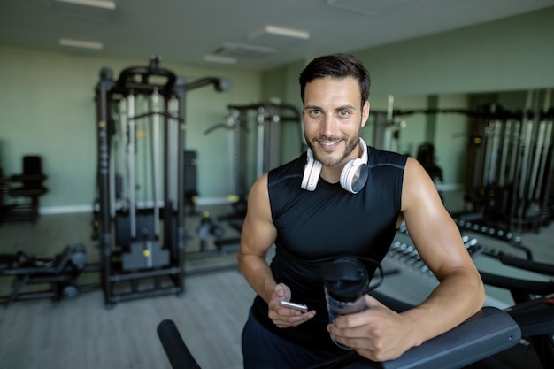 Foto grátis jovem atleta feliz usando telefone celular enquanto trabalhava no health club