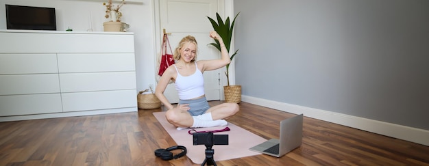 Foto grátis jovem atleta, instrutora de fitness, mulher senta-se no tapete de borracha do chão gravando vídeo digitalmente