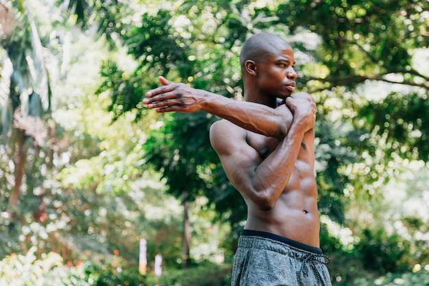 Jovem atleta musculoso, esticando a mão na frente de árvores