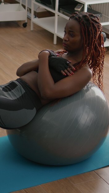 Jovem atlética fazendo exercícios matinais de fitness na sala de estar, exercitando o músculo abdominal, sentada na bola suíça de ioga