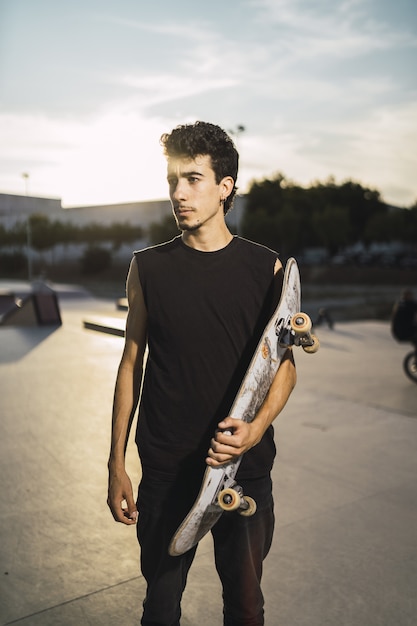 Jovem atlético com uma camisa preta segurando um skate olhando para o lado