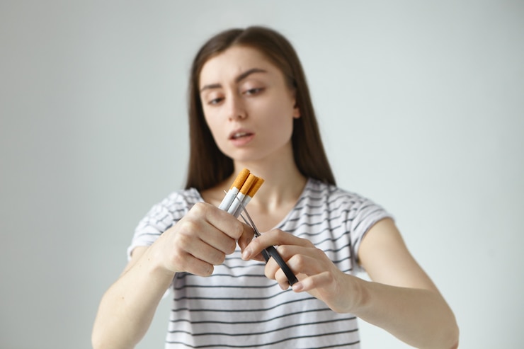 Foto grátis jovem atraente de cabelos escuros em uma camiseta listrada segurando um monte de cigarros e tesouras, cortando-os ao meio enquanto decidia parar de fumar e abandonar o mau hábito para sempre. foco seletivo